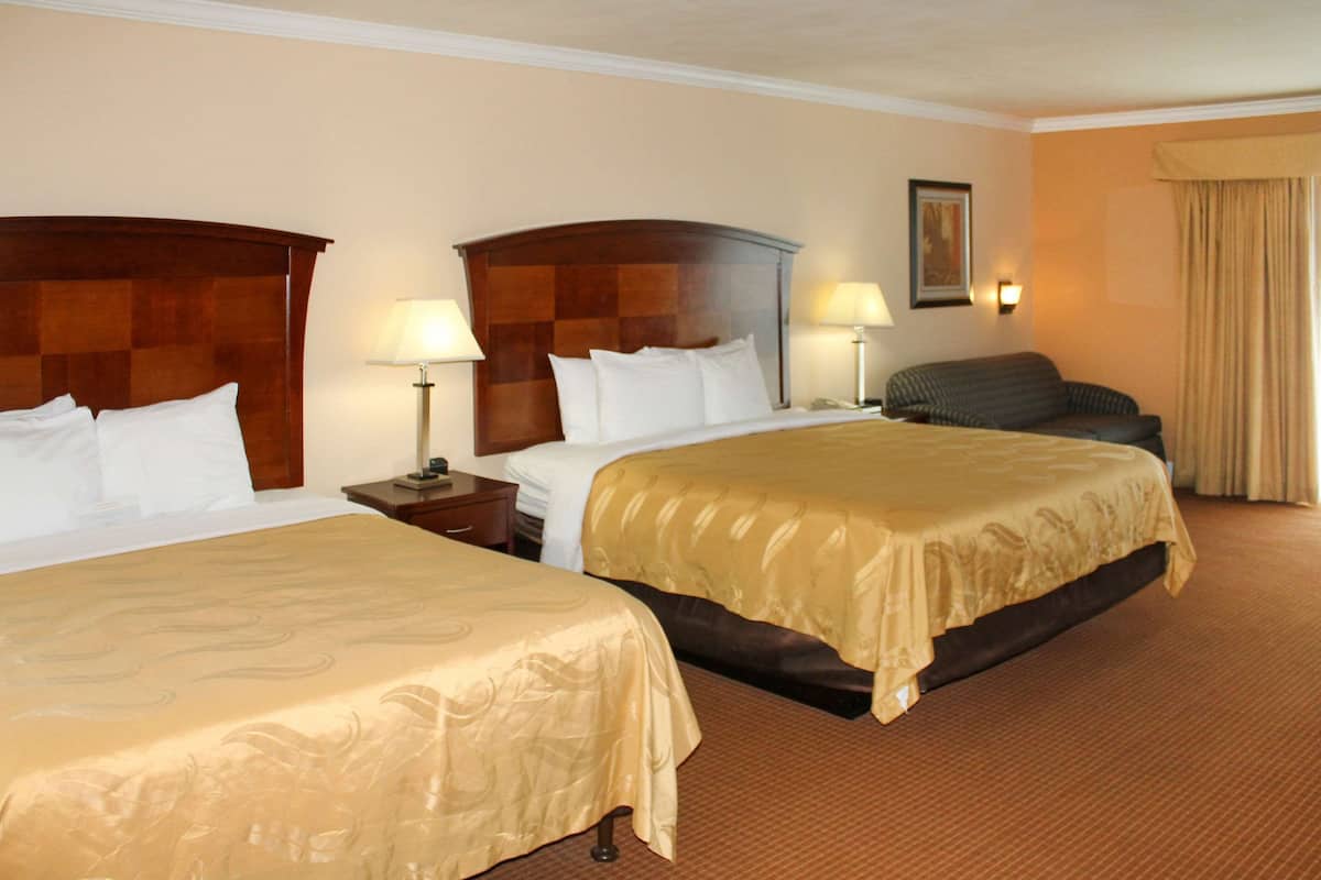 A hotel room with two double beds, a sofa, a nightstand with a lamp, and a framed picture on the wall.