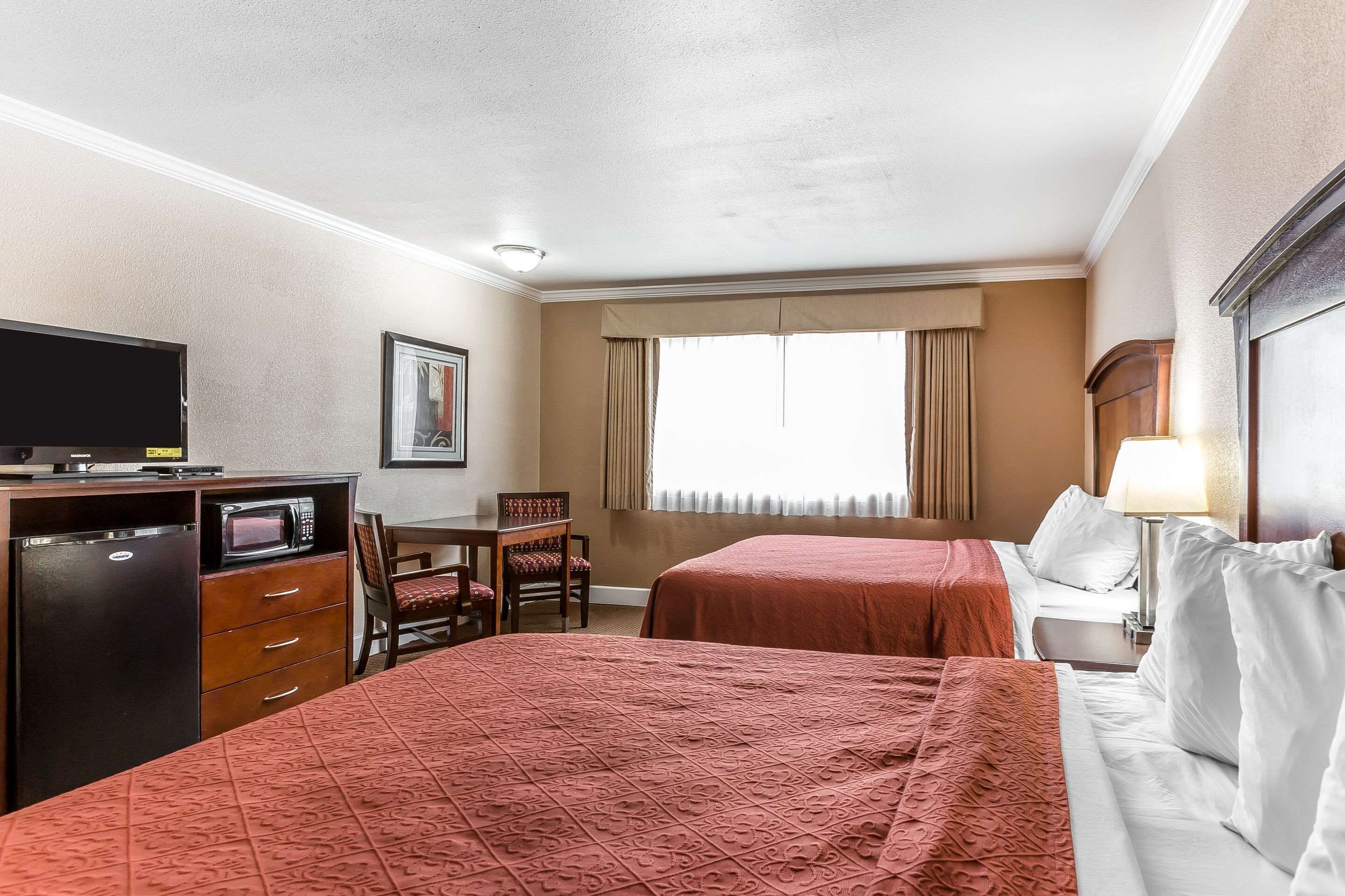 Habitación de hotel con dos camas, un escritorio con televisor, microondas y una silla.