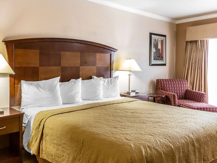 A hotel room with a large bed, two bedside lamps, a chair, and a framed picture on the wall.