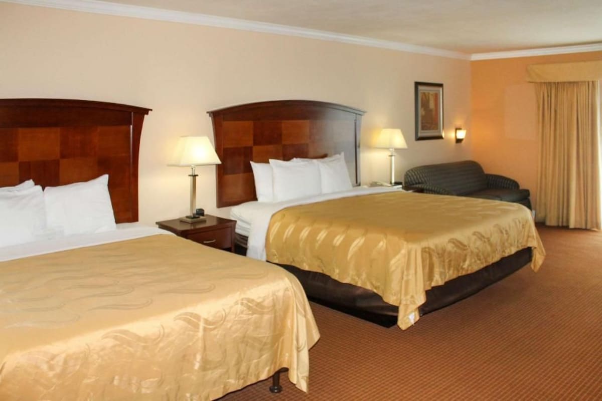 Une chambre d’hôtel avec deux lits, un canapé, une table de chevet et une lampe.