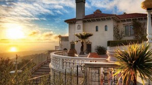 A grand building with a stone staircase leading to a balcony, surrounded by lush greenery and a clear sky. - Quality Inn near Hearst Castle (San Simeon)