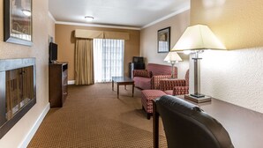 A hotel room with a checkered carpet, a sofa set, a desk, a lamp, a television, and a fireplace. - Quality Inn near Hearst Castle (San Simeon)