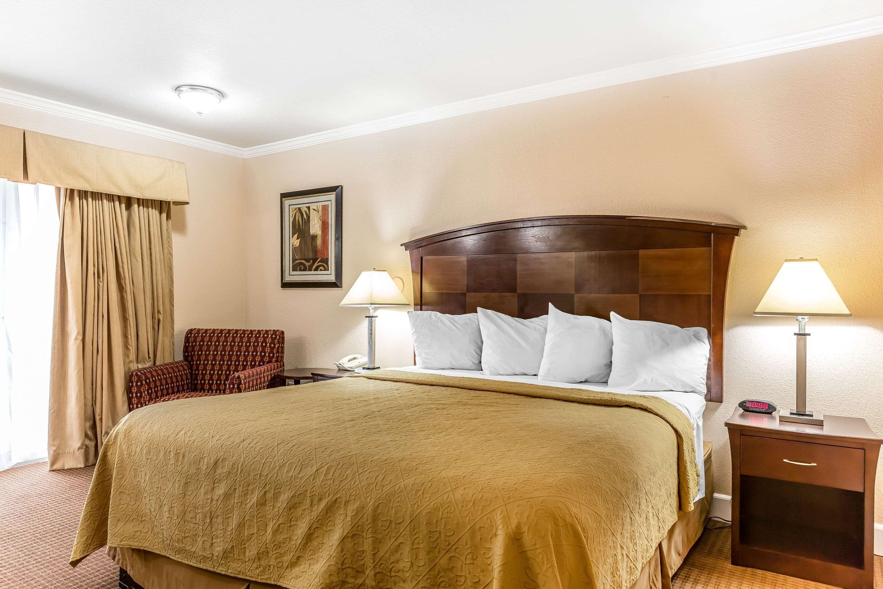 A hotel room with a large bed, two bedside lamps, a nightstand, a chair, and a painting on the wall.