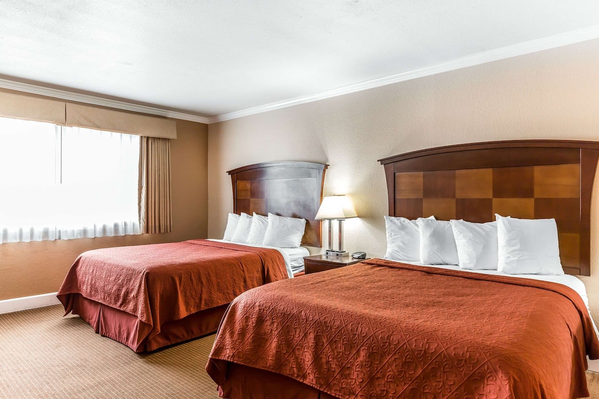 A hotel room with two beds, beige walls, and a large window with curtains.