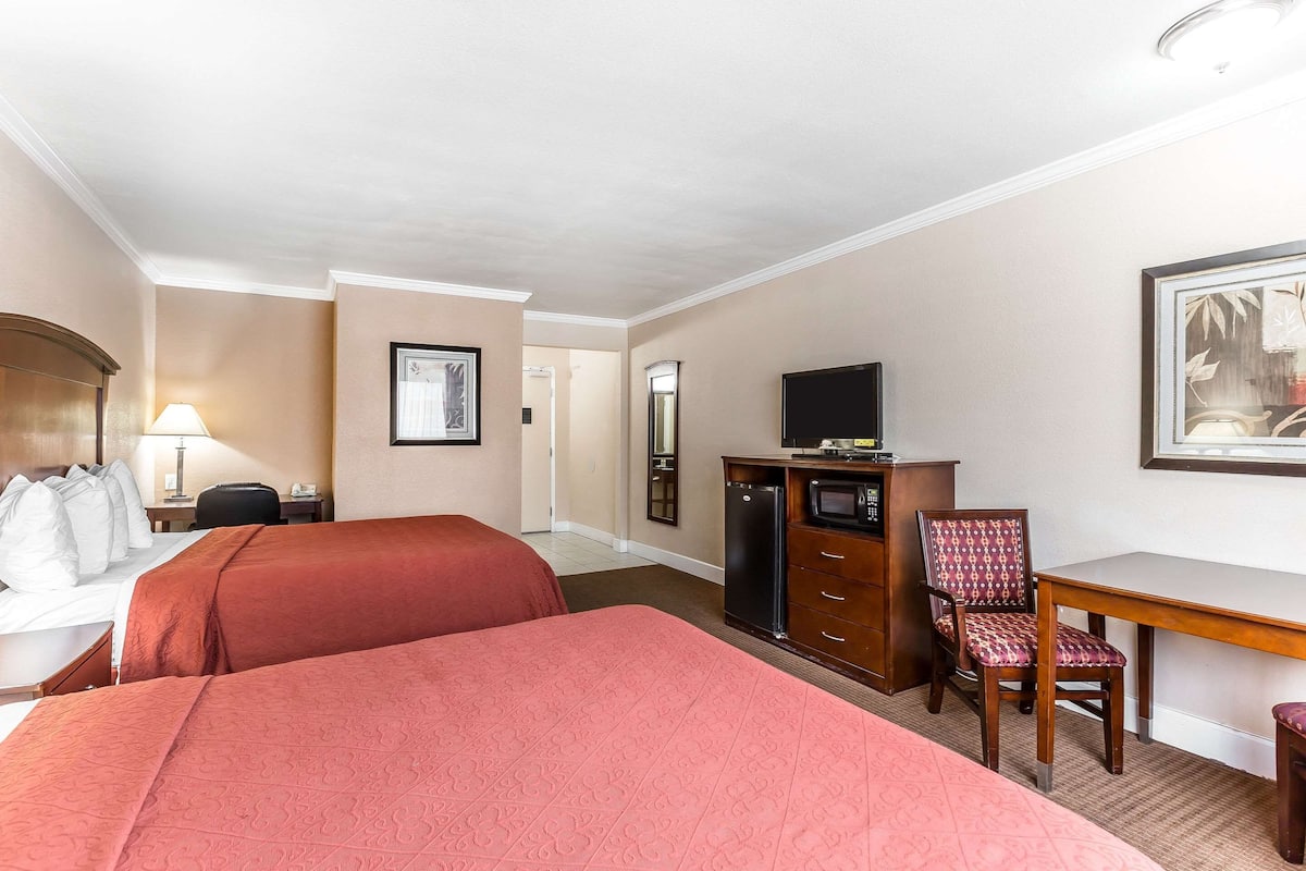 A hotel room with two beds, a desk, a television, and a chair.