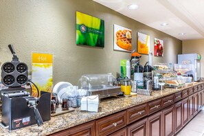 A breakfast buffet area with a waffle maker, coffee station, and various food items. - Quality Inn near Hearst Castle (San Simeon)