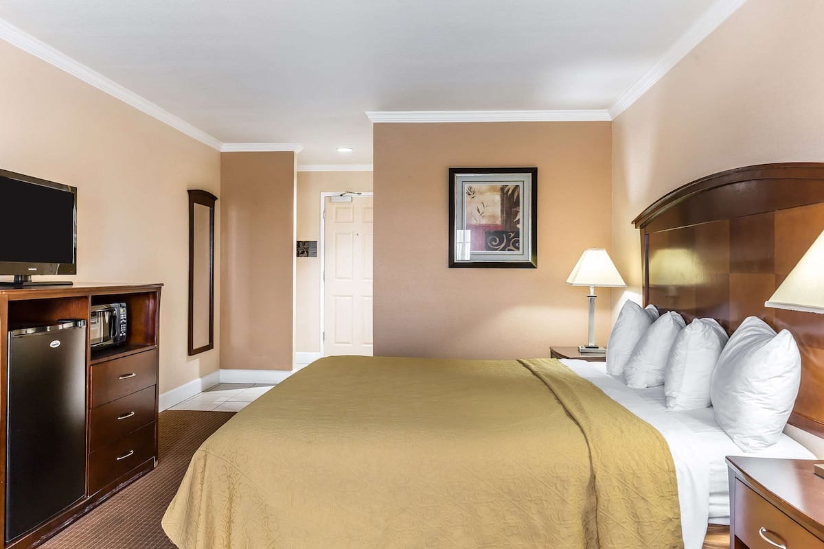 A hotel room with a bed, a desk with a television, a microwave, and a door leading to another room.