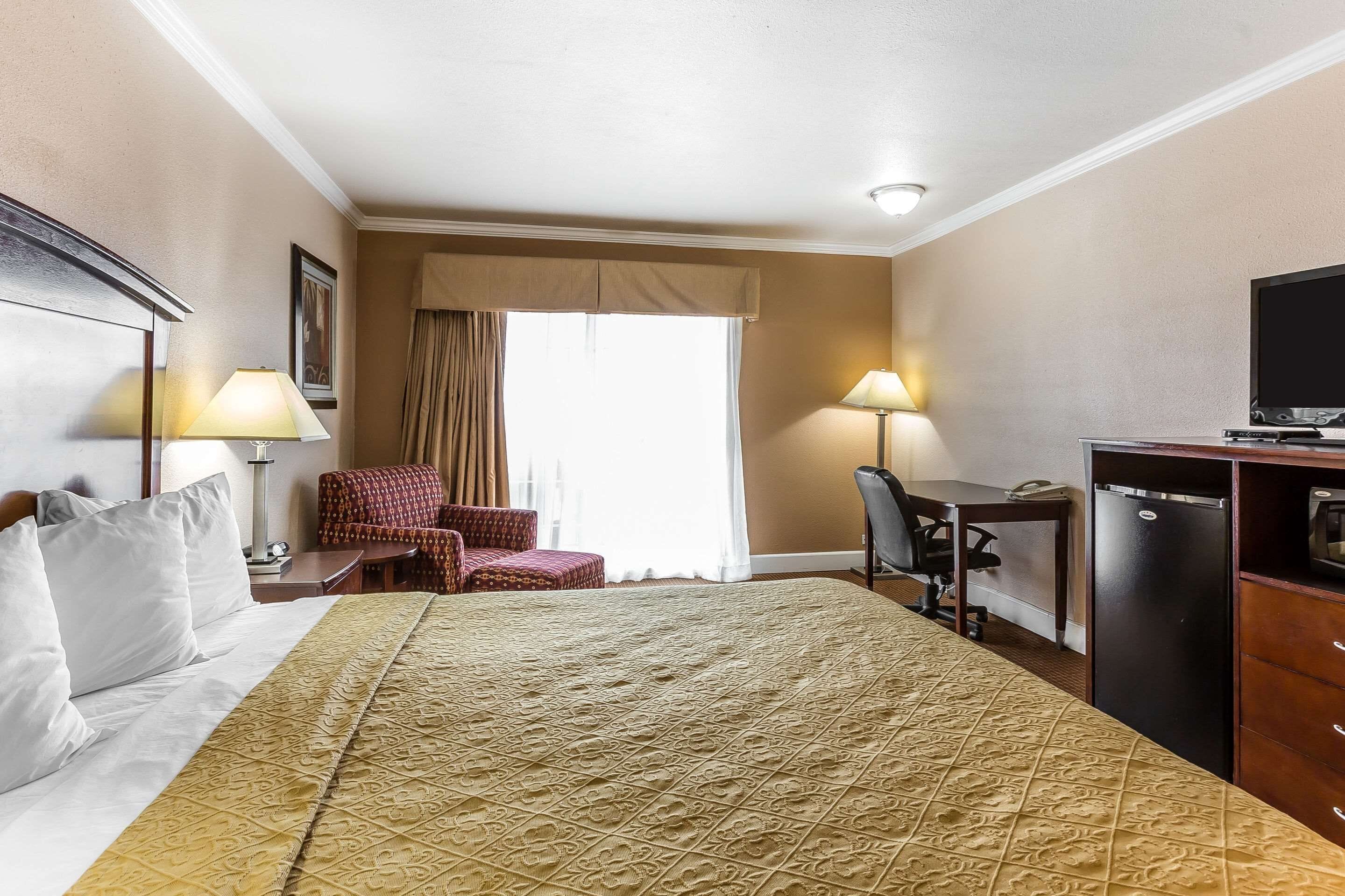 Habitación de hotel con cama, escritorio, silla, televisor y refrigerador.