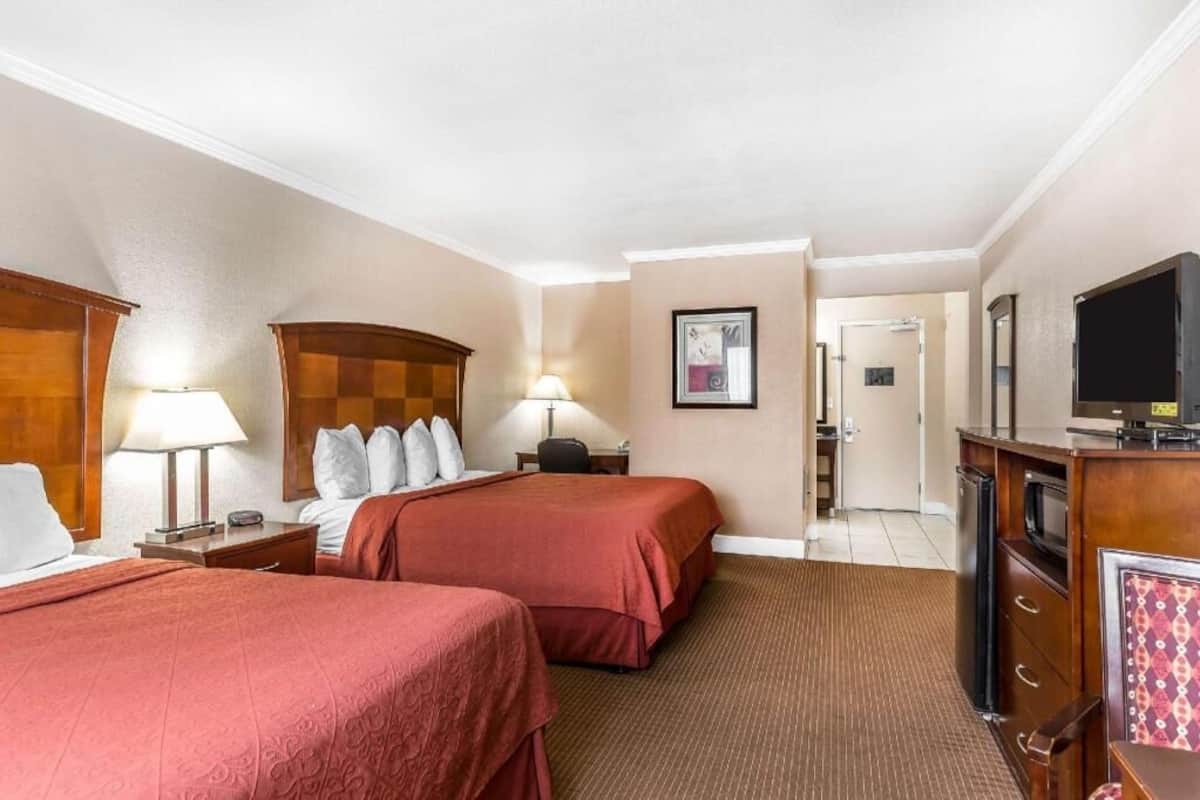 A hotel room with two beds, a desk, a television, and a door leading to a hallway.