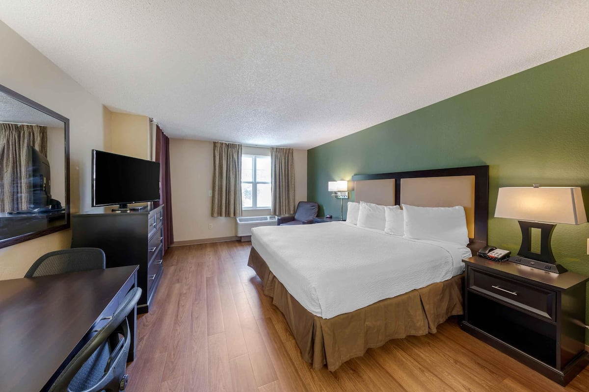 Une chambre d’hôtel avec un grand lit, un bureau, une télévision et une fenêtre avec des rideaux.