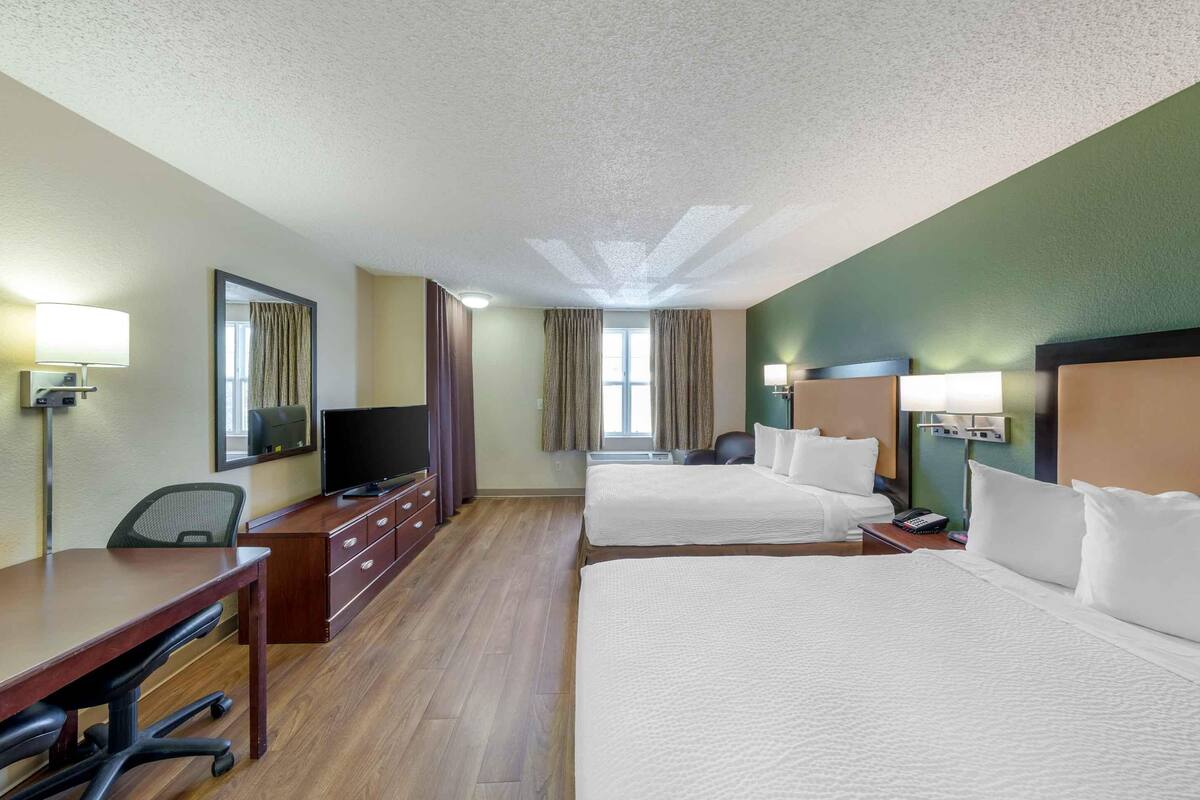 Une chambre d’hôtel avec deux lits, un bureau, une chaise, une télévision et une fenêtre avec des rideaux.