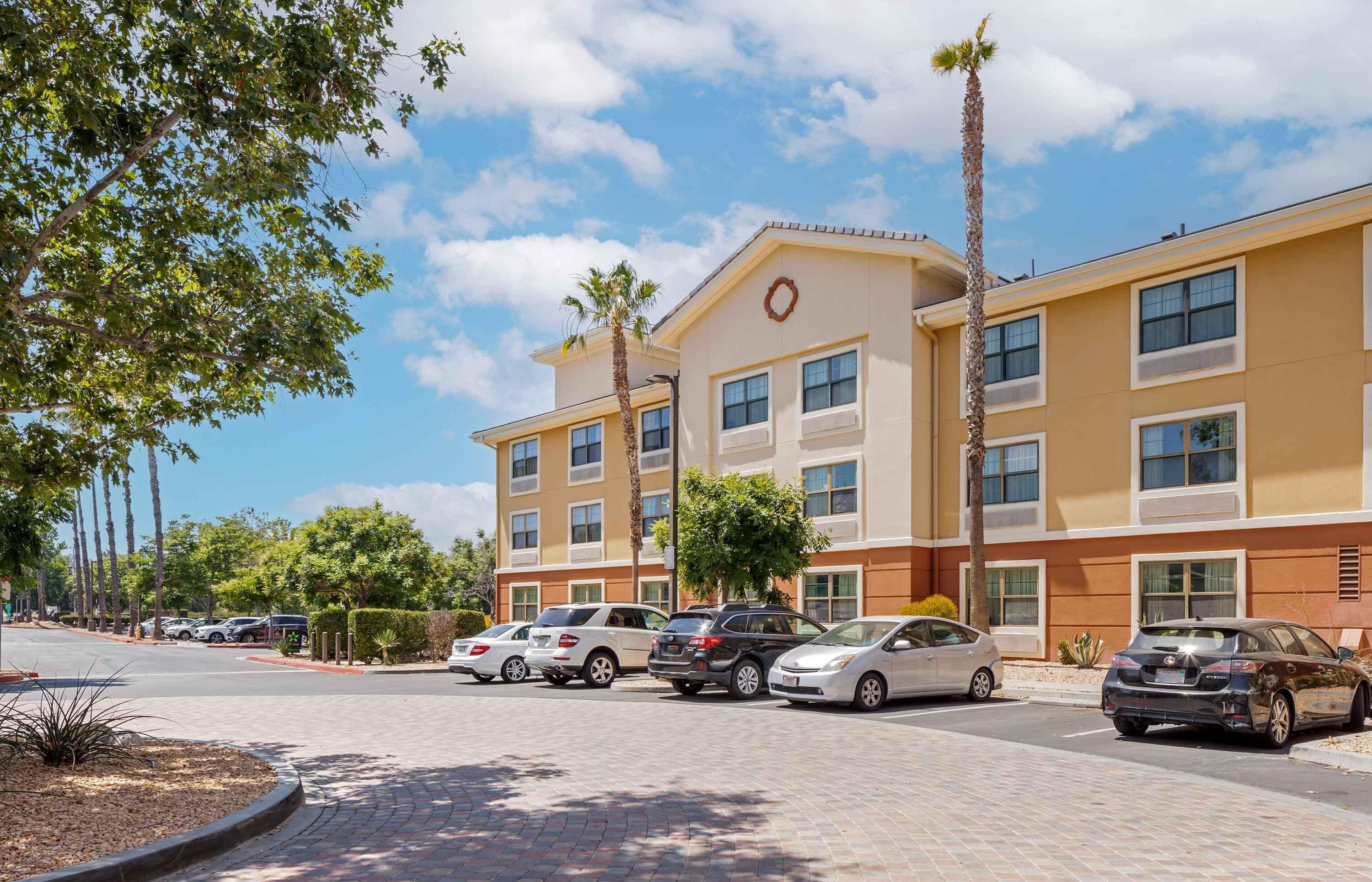 A multi-story hotel with a beige facade, multiple windows, and a parking lot with several cars.