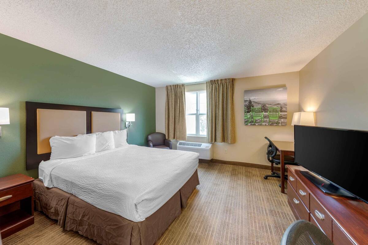 Une chambre d’hôtel avec un grand lit, un téléviseur à écran plat, un bureau avec une lampe et une fenêtre avec des rideaux.