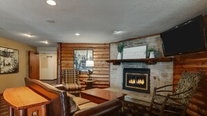 Un acogedor interior de cabaña de troncos con chimenea, muebles de madera y un televisor montado en la pared.