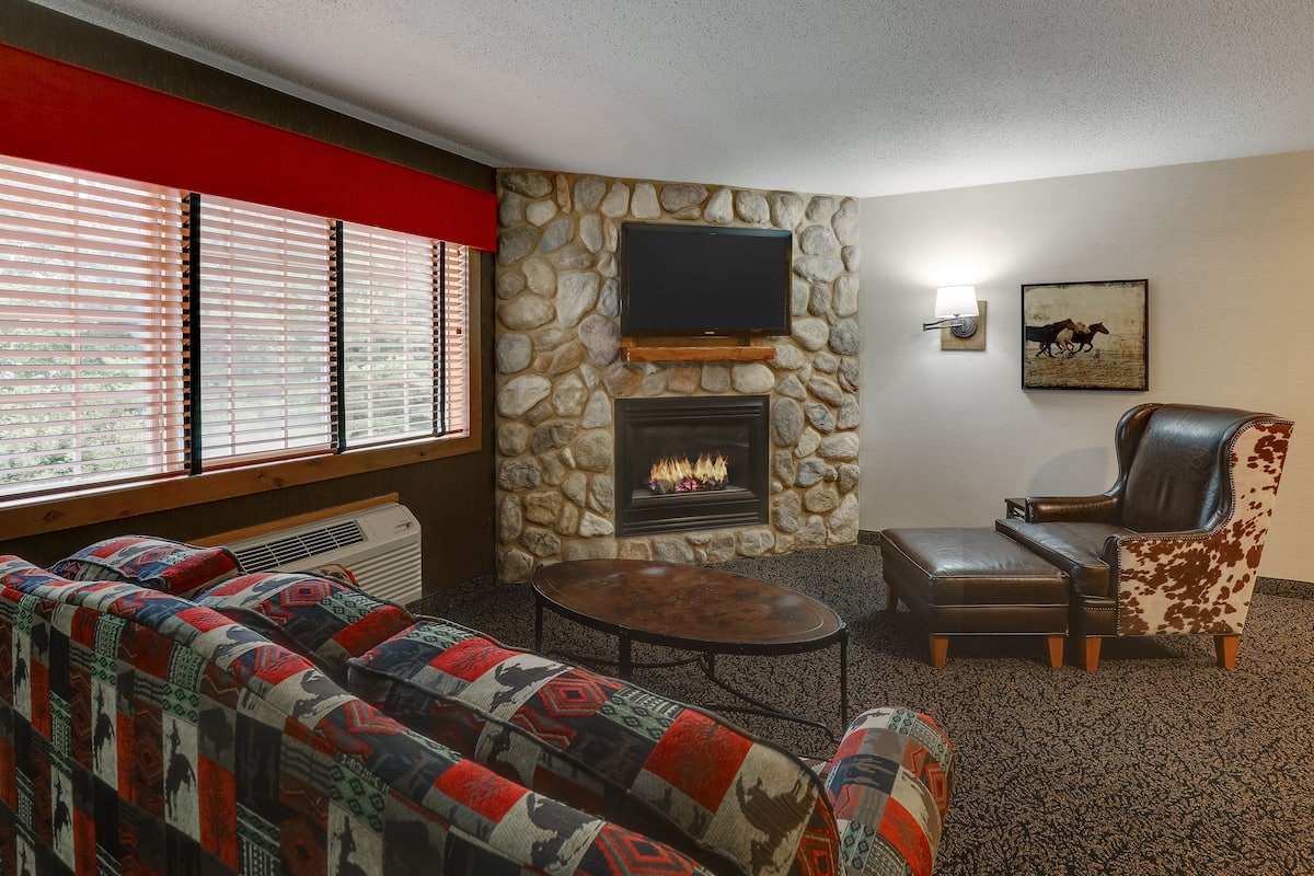 A living room with a stone fireplace, a television mounted above it, and a leather armchair.