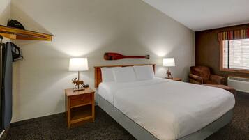 A hotel room with a large bed, two bedside lamps, a wooden nightstand, a chair, and a window with blinds.