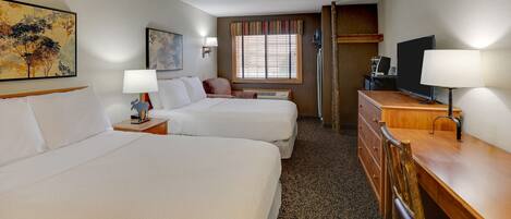 A hotel room with two beds, a desk, a television, and a window with blinds.