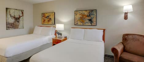 Habitación de hotel con dos camas, una mesita de noche con lámpara, una silla y obras de arte en las paredes.