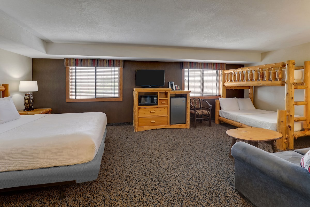 A hotel room with two beds, a desk with a television, a small table, and a bunk bed.