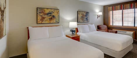 A hotel room with two beds, a nightstand with a lamp, a decorative cow figurine, and artwork on the walls.