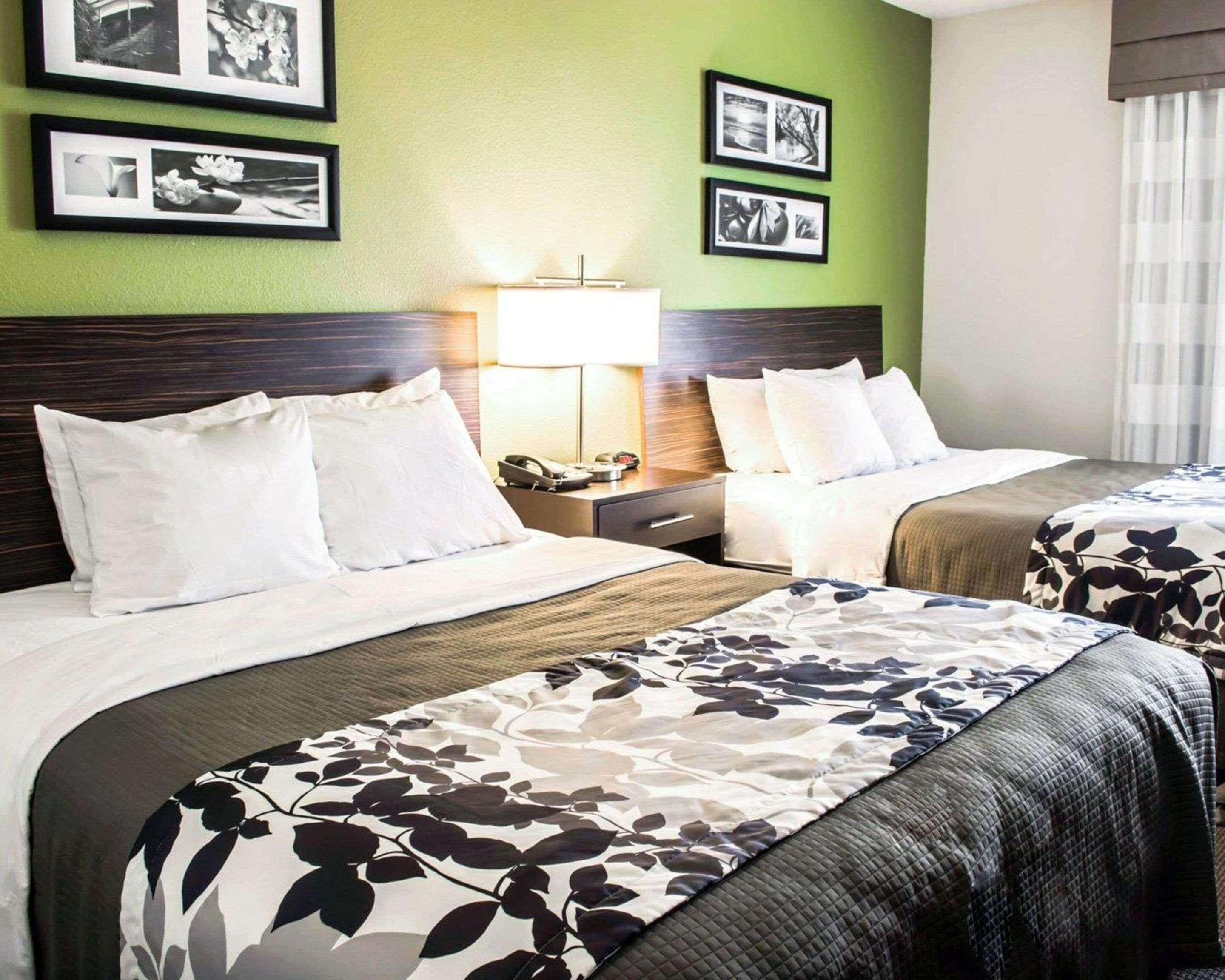 A hotel room with two beds, a nightstand, a lamp, and framed pictures on the wall.