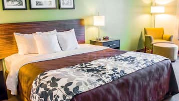 A hotel room with a large bed, a nightstand with a lamp, a chair, and framed pictures on the wall.