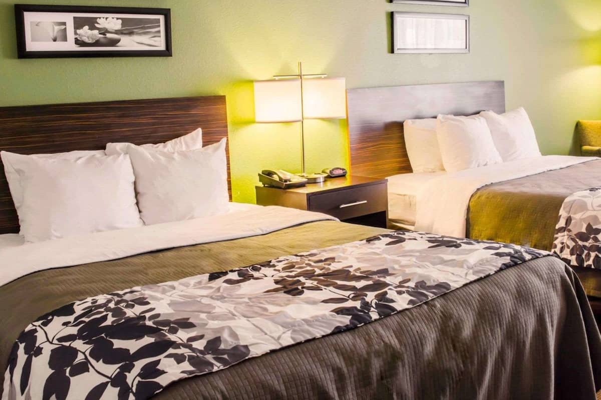 A hotel room with two beds, a wooden headboard, a nightstand with a lamp, and framed pictures on the wall.