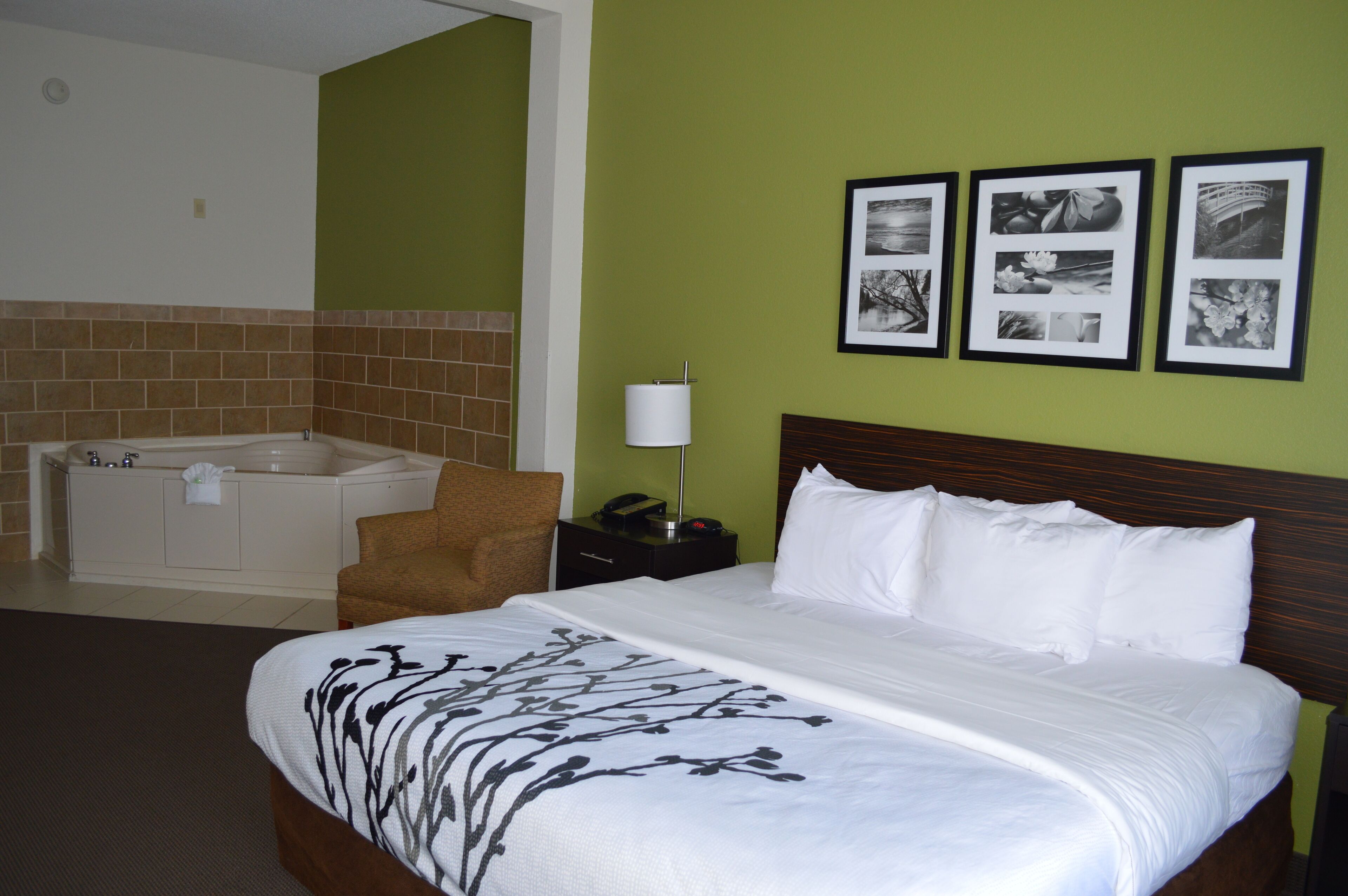 Une chambre d’hôtel avec un grand lit, un coin salon avec un fauteuil, une baignoire et une table de chevet avec une lampe.
