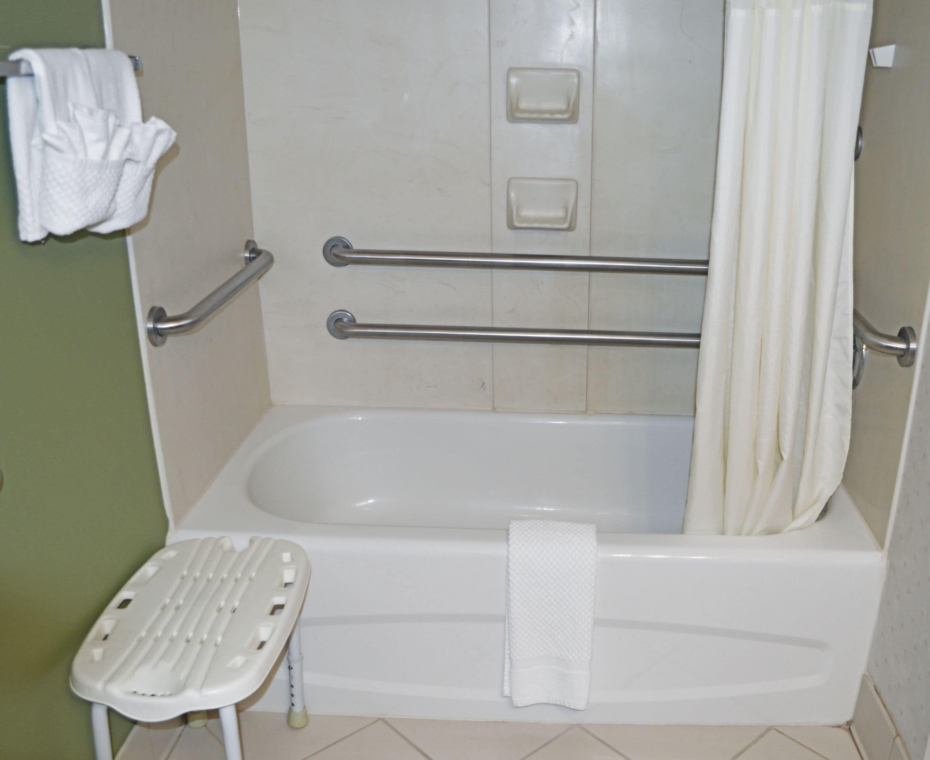A standard bathroom with a bathtub, grab bars, a white shower curtain, and a white towel on the wall.