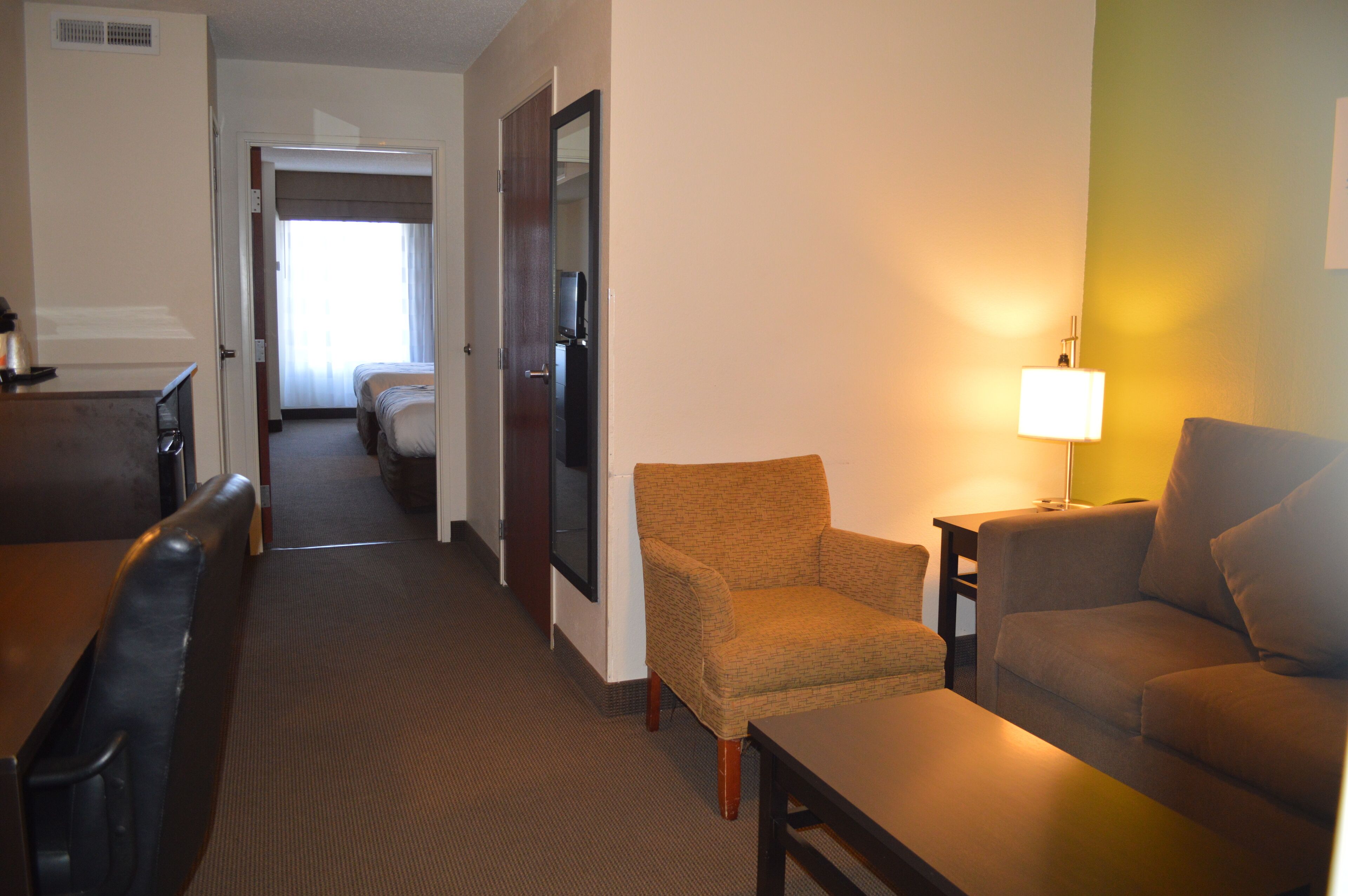 A hotel room with a bed, a desk, a chair, a sofa, and a lamp.