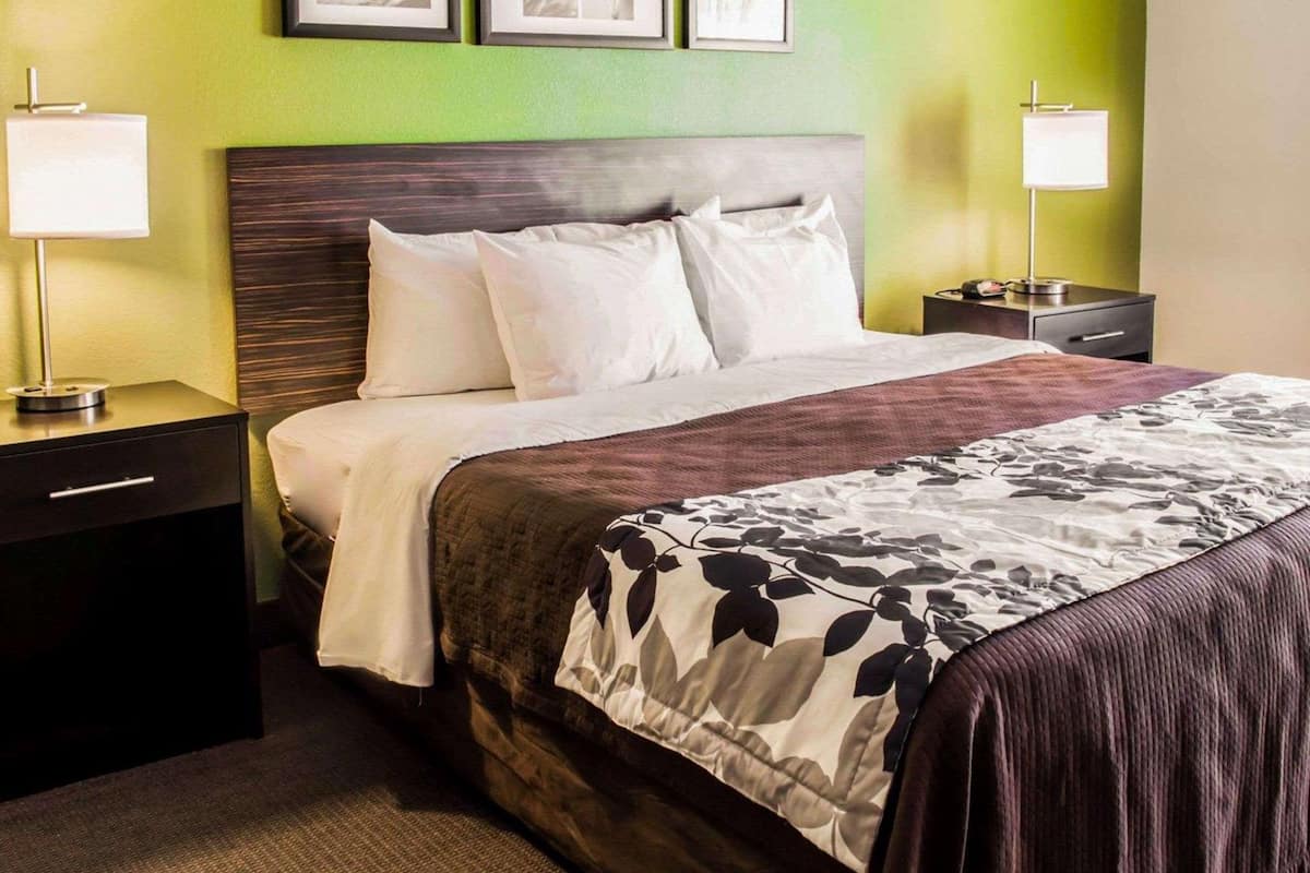A hotel room with a bed, two bedside tables, a nightstand, and a wall with framed pictures.