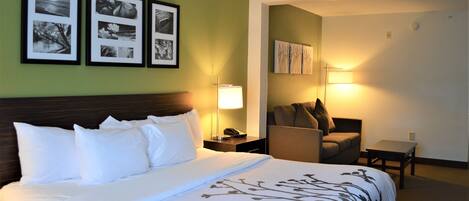 Habitación de hotel con una cama grande, una mesita de noche con lámpara, una silla y cuadros en la pared.