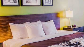Un lit bien fait, avec des draps blancs et un couvre-lit à motifs floraux, une tête de lit en bois foncé et une table de chevet avec une lampe et une horloge.