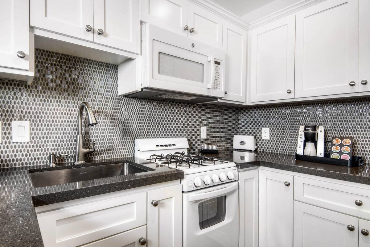 A modern kitchen with white cabinets, a stainless steel stove, a microwave, and a coffee maker.