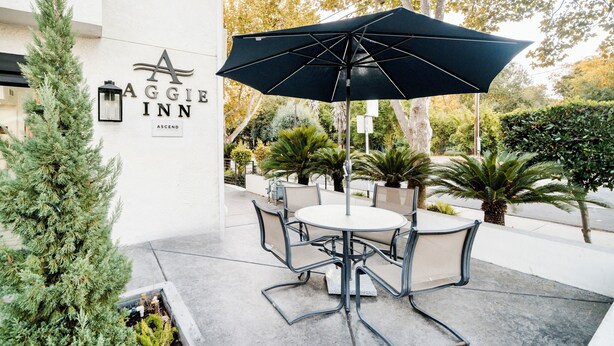 An outdoor seating area with a table and chairs, an umbrella, and a sign for 'Aggiie Inn'. - Aggie Inn, an Ascend Collection Hotel (Davis)