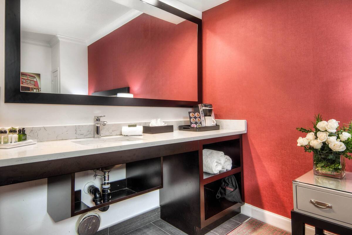 A modern bathroom with a large mirror, white sink, and a red accent wall.