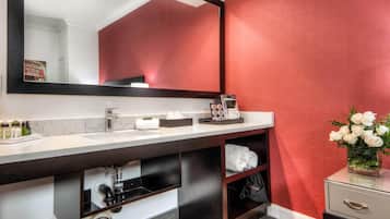 A modern bathroom with a large mirror, white sink, and a red accent wall.