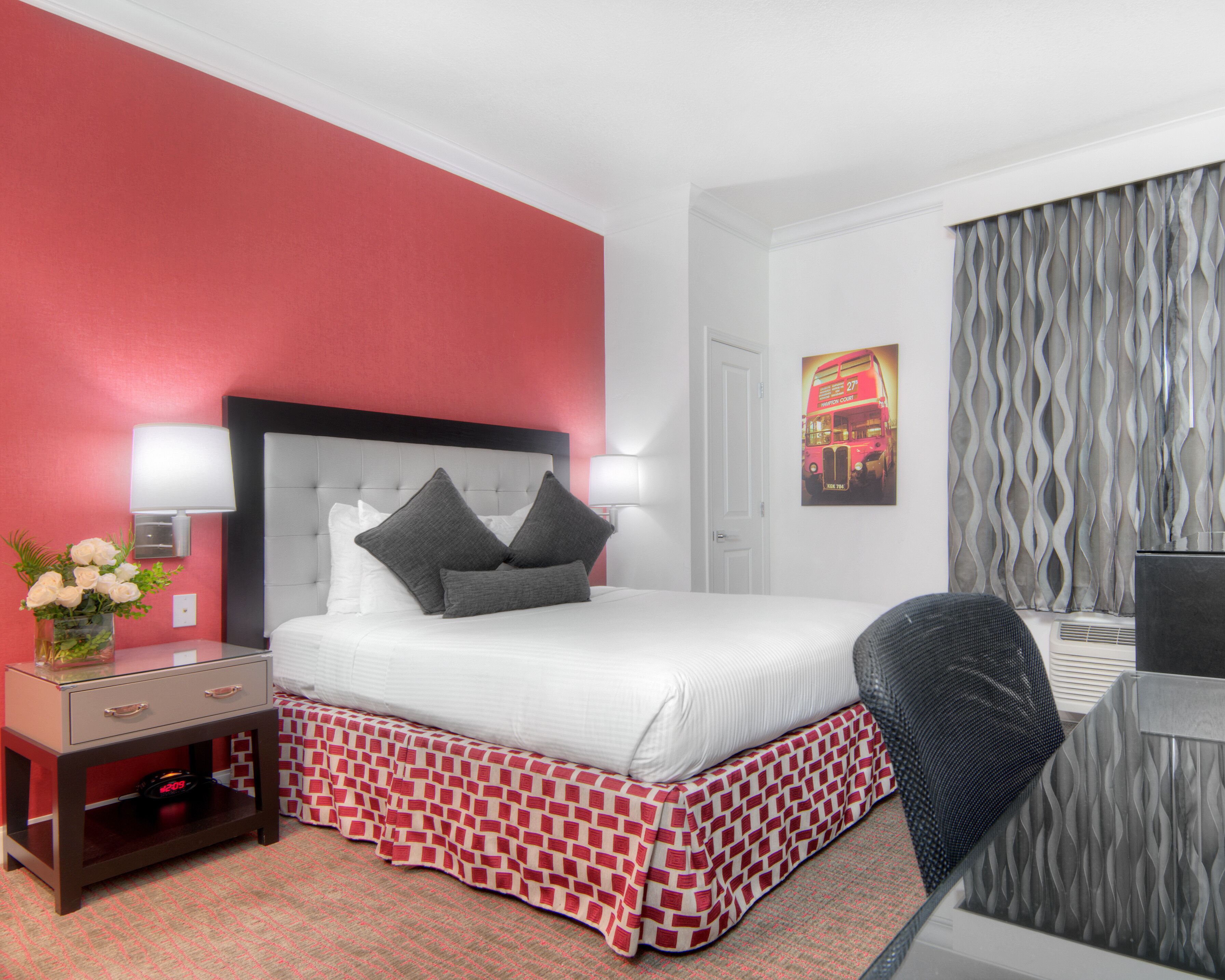 A hotel room with a bed, bedside table, lamp, and a poster on the wall.