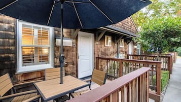 Una terraza de madera con una mesa, sillas, un paraguas negro y una puerta blanca.