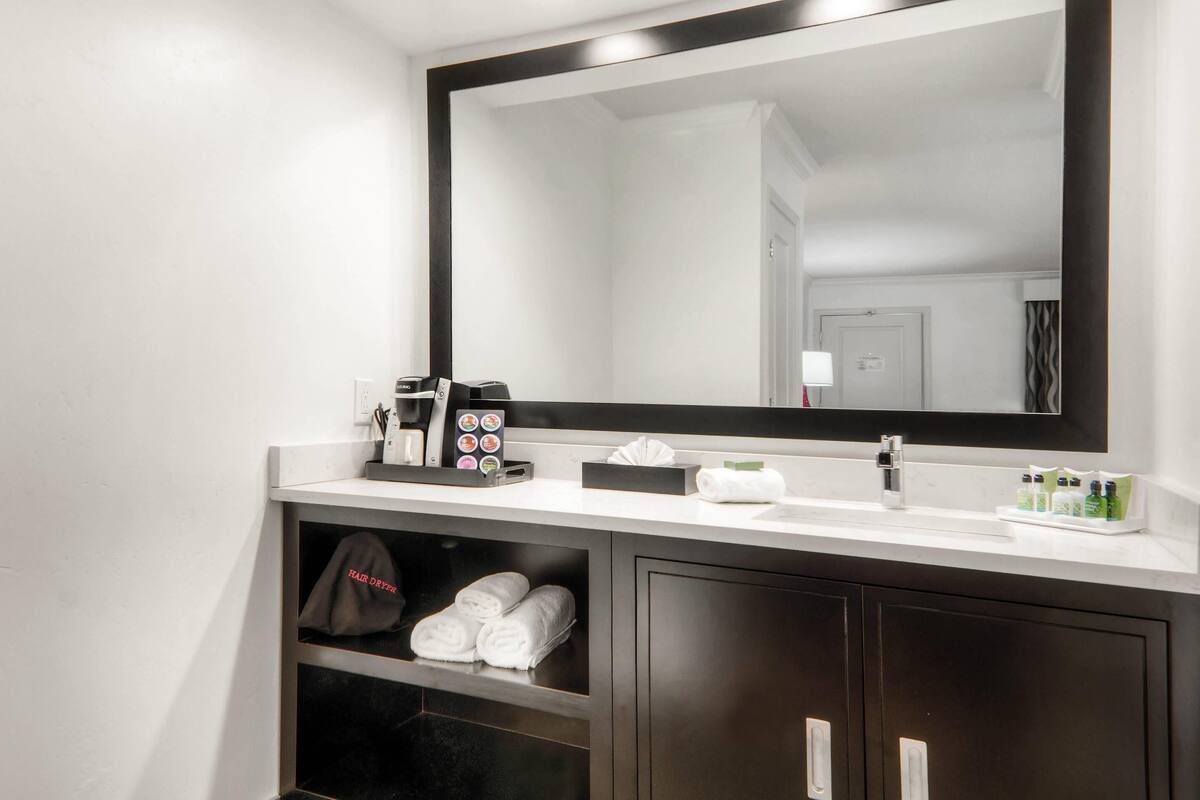 A modern bathroom with a large mirror, a white sink, and a towel rack.