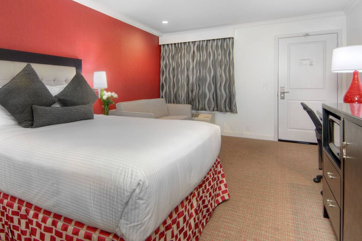 A hotel room with a bed, a desk, a chair, a dresser, and a door.