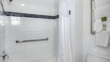 A modern bathroom with a white tiled shower, a grab bar, a toilet, and a towel rack.