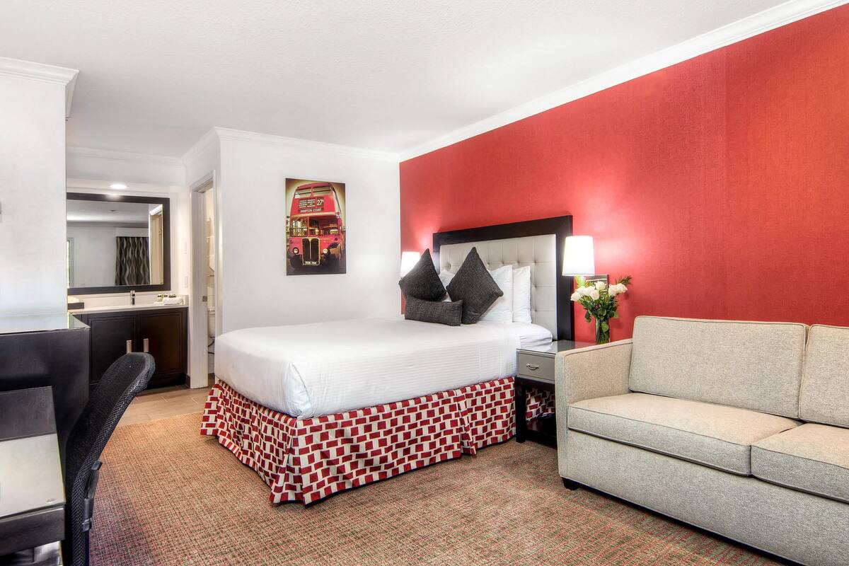 A hotel room with a bed, a sofa, a desk, and a mirror.