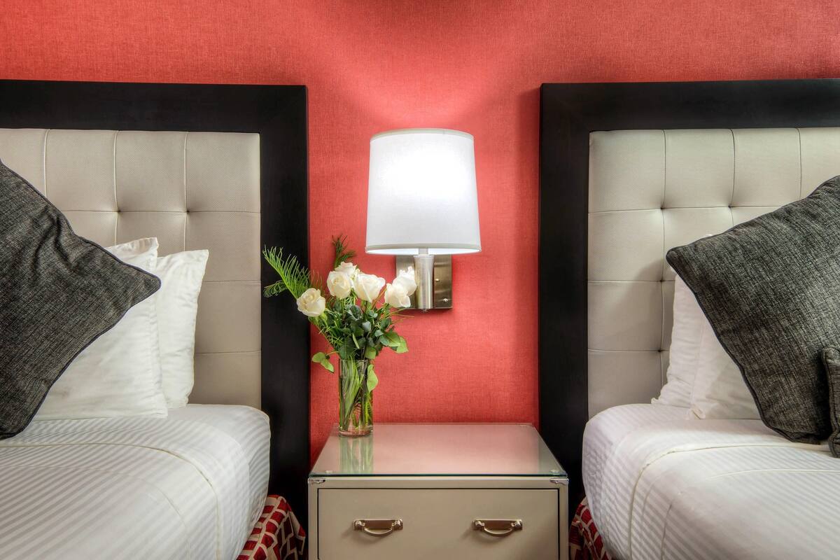 A hotel room with two beds, a nightstand with a lamp, and a vase with flowers.