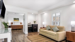 A modern living room with a sofa, a coffee table, and a TV. There is a kitchen area with cabinets and a microwave. - Aggie Inn, an Ascend Collection Hotel (Davis)