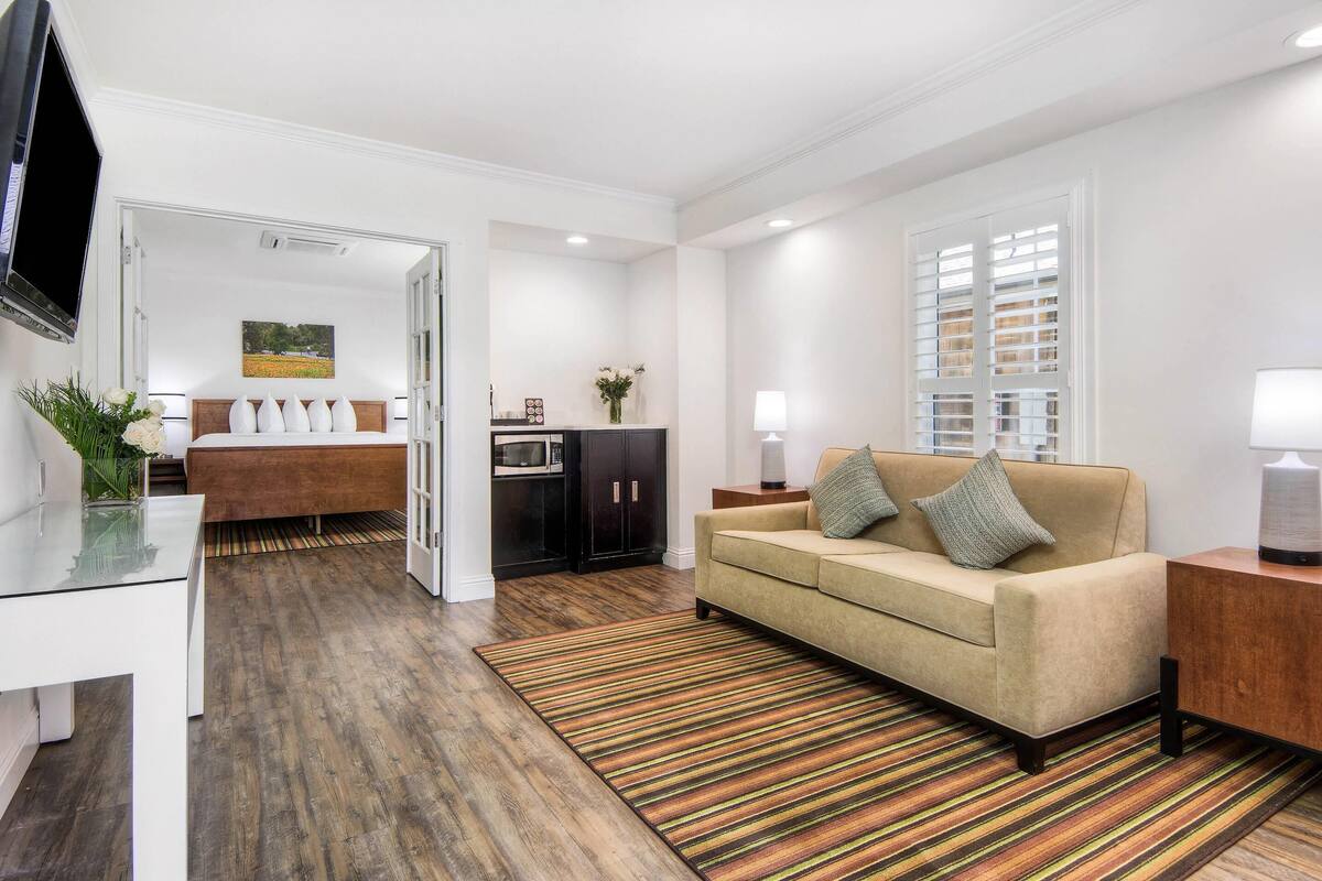 A modern living room with a sofa, a coffee table, and a TV. There is a kitchen area with cabinets and a microwave.
