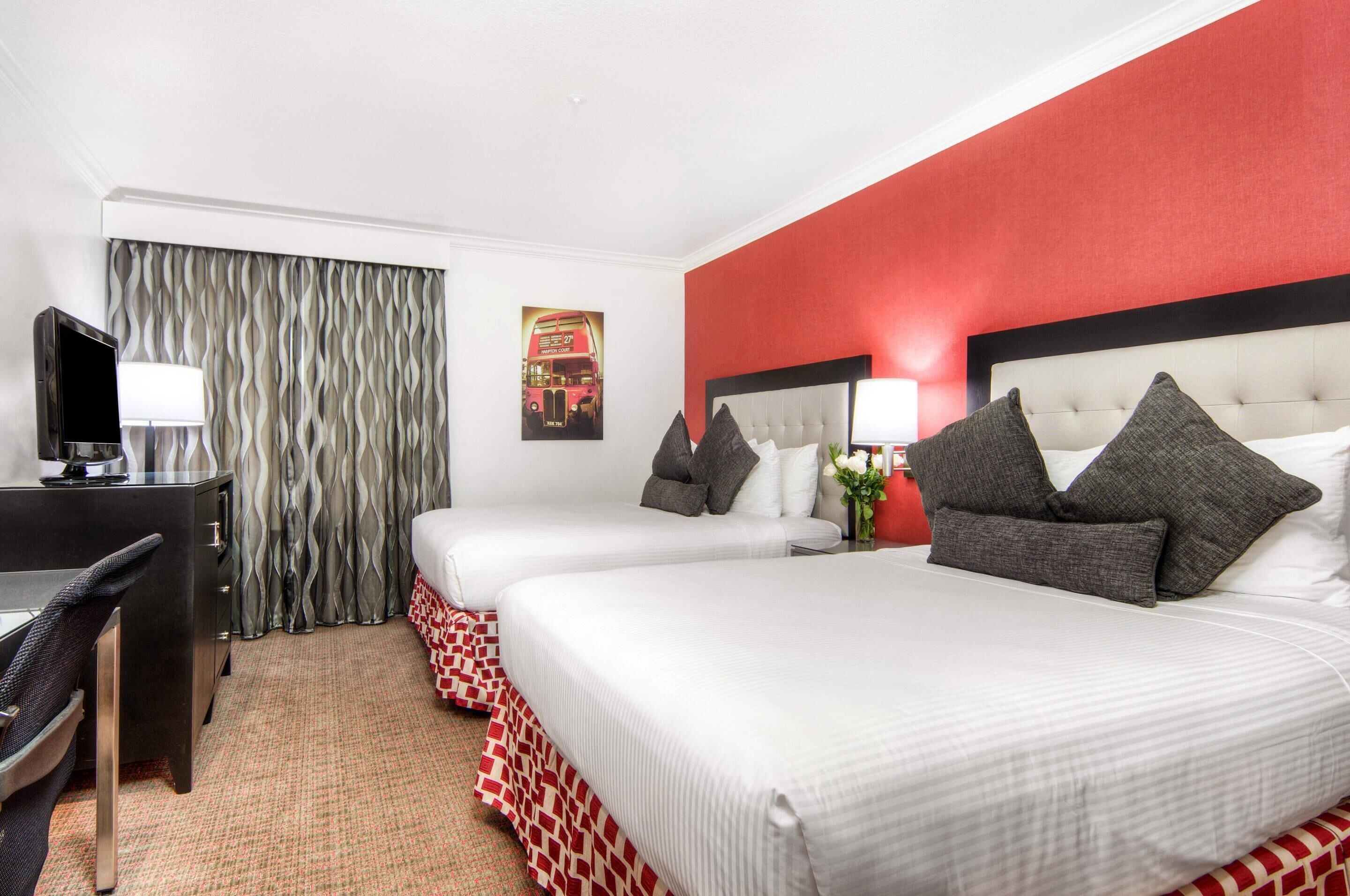 A hotel room with two beds, a desk, a chair, and a television.