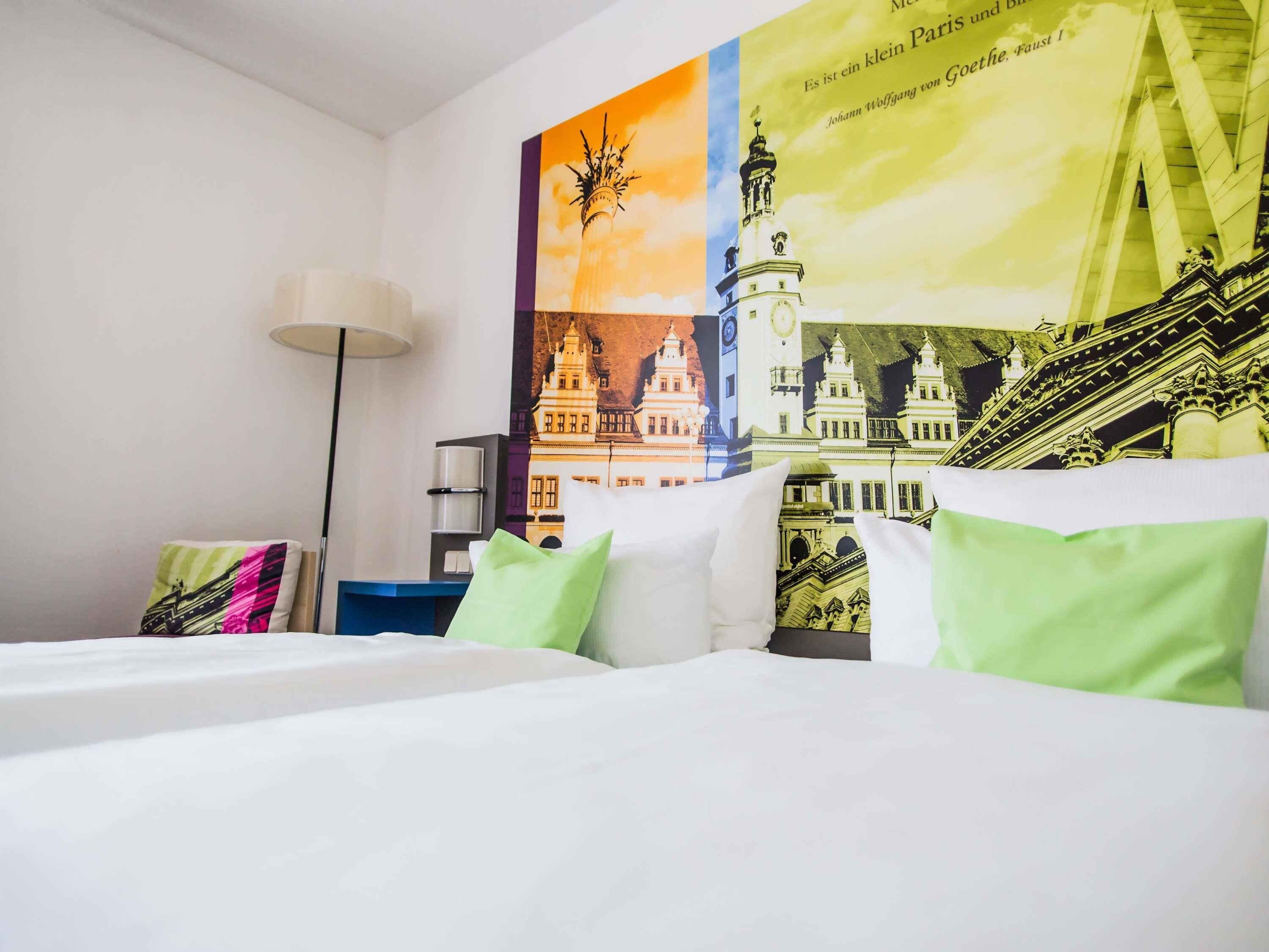 A hotel room with a bed, pillows, a lamp, and a wall with a cityscape poster.
