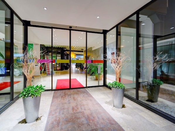 A modern entrance with glass doors, a red carpet, and potted plants. - ibis Styles Leipzig (Schkeuditz)