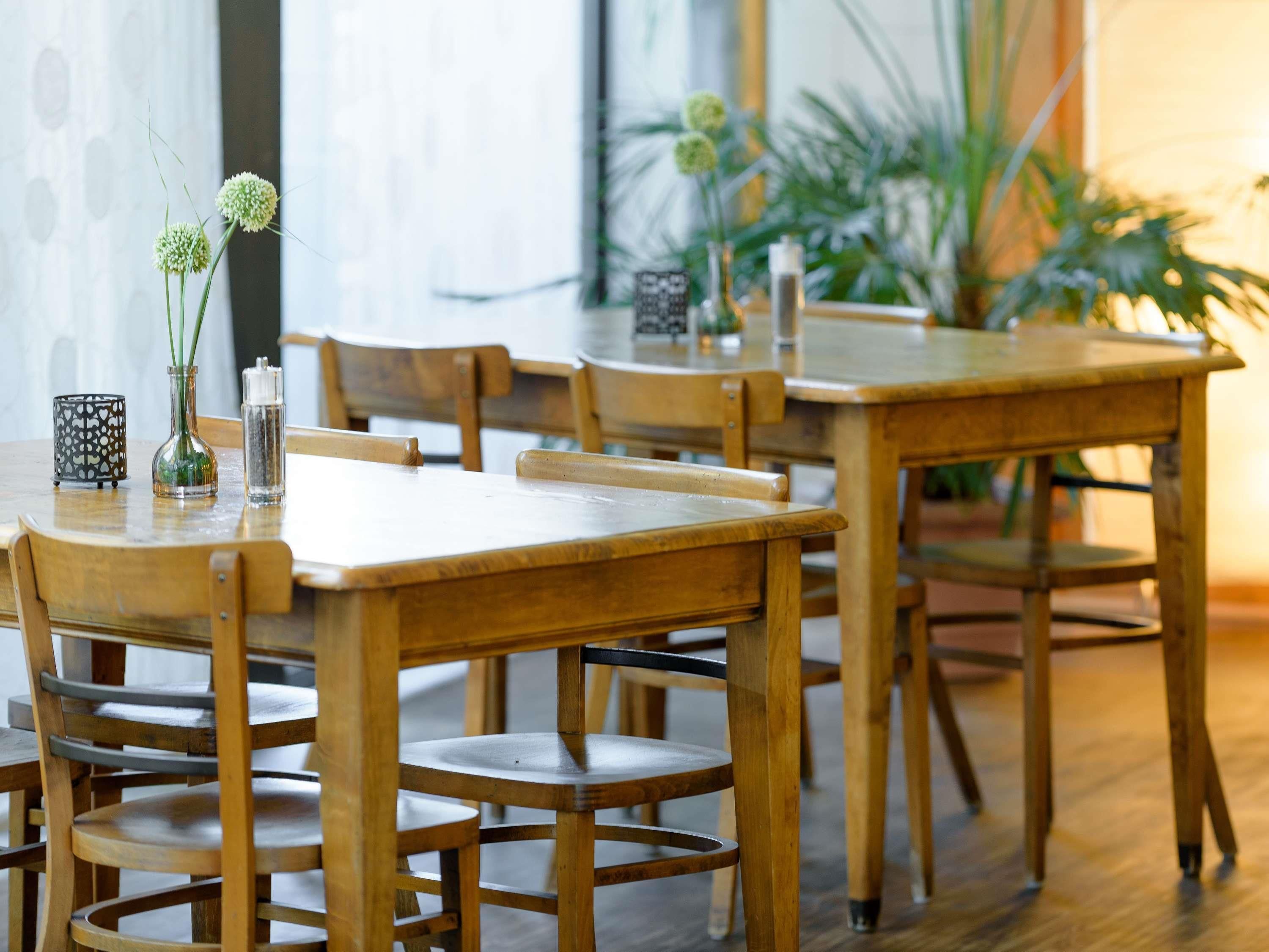 Een eetgedeelte met houten tafels en stoelen, een vaas met bloemen en een patroonhouder voor kaarsen.